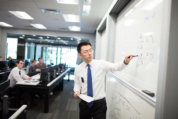 A business professor writing on a whiteboard. 